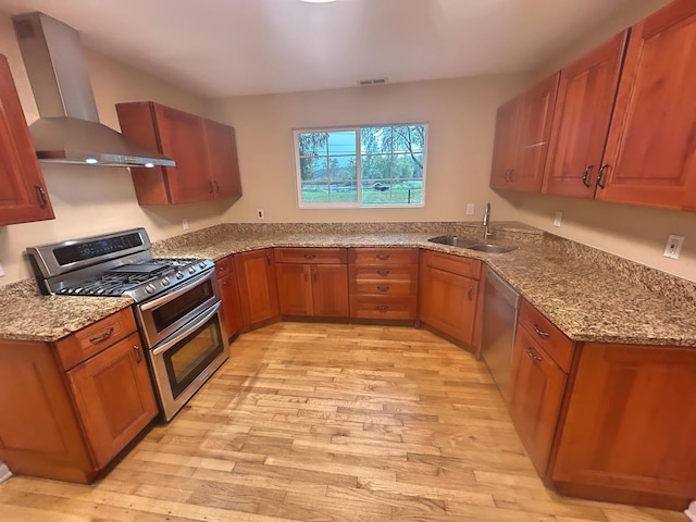 kitchen featuring light stone countertops, wall chimney exhaust hood, stainless steel appliances, light hardwood / wood-style floors, and sink