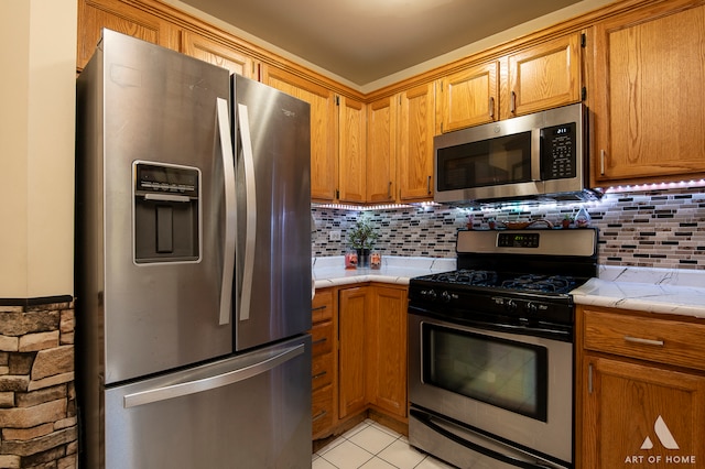 kitchen featuring appliances with stainless steel finishes, tasteful backsplash, light tile patterned floors, and tile counters