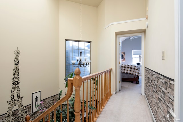 hallway featuring light carpet, a towering ceiling, and an inviting chandelier