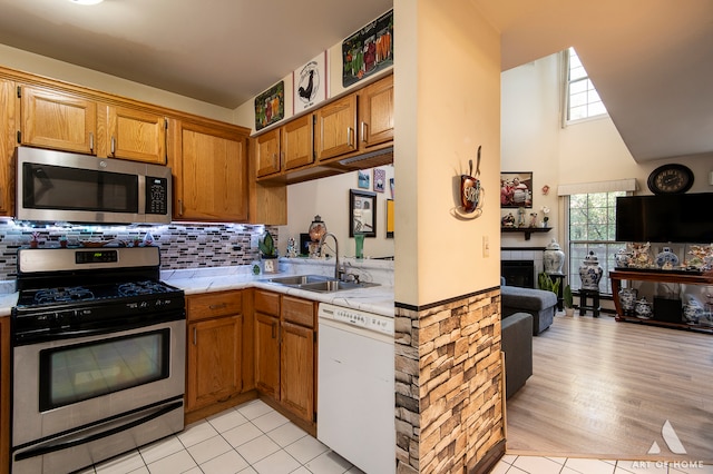 kitchen featuring decorative backsplash, appliances with stainless steel finishes, sink, a high ceiling, and light hardwood / wood-style floors