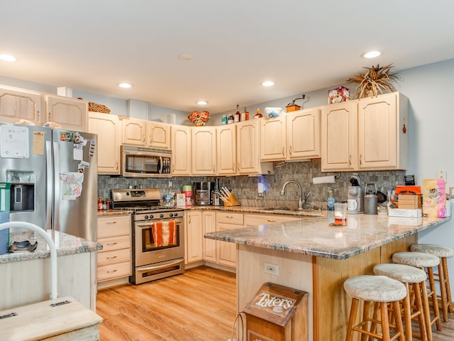 kitchen featuring appliances with stainless steel finishes, light stone counters, kitchen peninsula, a breakfast bar area, and light hardwood / wood-style flooring