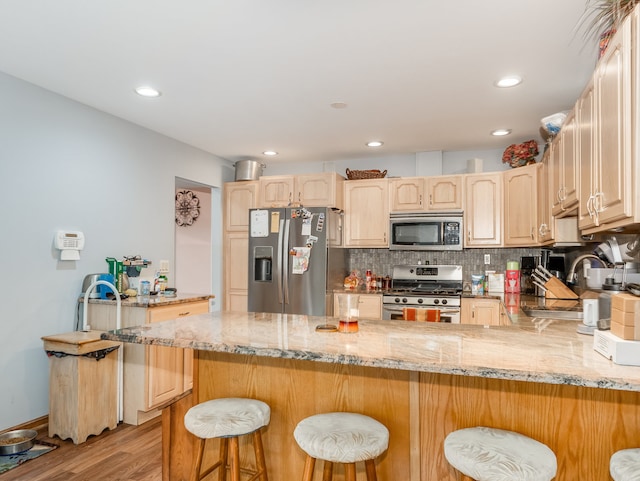 kitchen featuring light wood-type flooring, kitchen peninsula, stainless steel appliances, a breakfast bar area, and light stone countertops