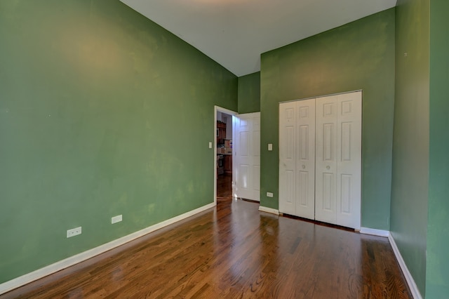 unfurnished bedroom with high vaulted ceiling, a closet, and dark hardwood / wood-style flooring