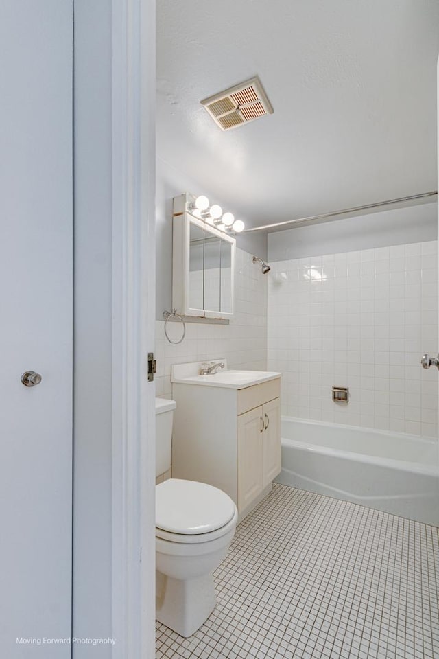 full bathroom with tile patterned flooring, tile walls, tiled shower / bath combo, vanity, and toilet