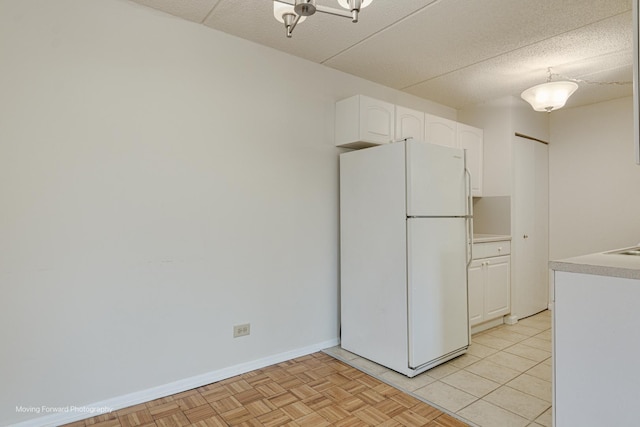 kitchen with white refrigerator, white cabinetry, light parquet flooring, and a textured ceiling