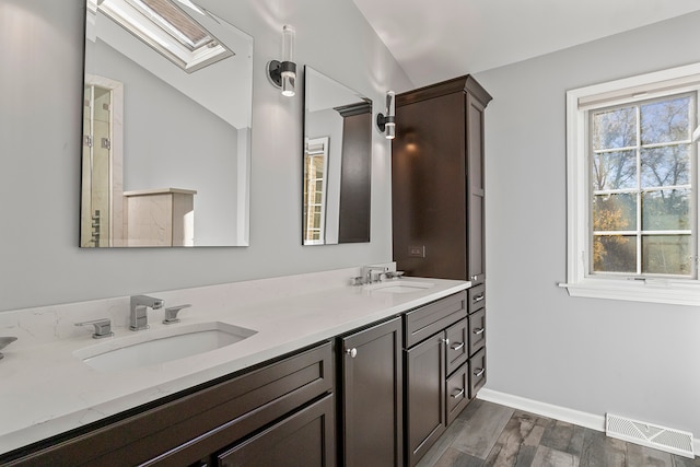 bathroom with vanity, vaulted ceiling with skylight, and hardwood / wood-style floors