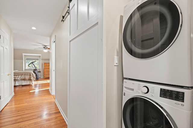 washroom featuring light wood-type flooring, a barn door, ceiling fan, and stacked washer / drying machine