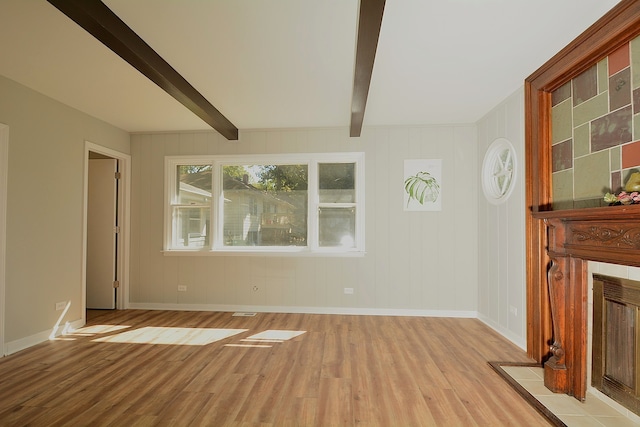 unfurnished living room featuring light hardwood / wood-style flooring, a tile fireplace, and beamed ceiling