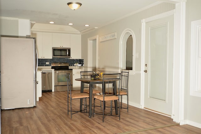 kitchen with appliances with stainless steel finishes, white cabinetry, backsplash, hardwood / wood-style flooring, and ornamental molding