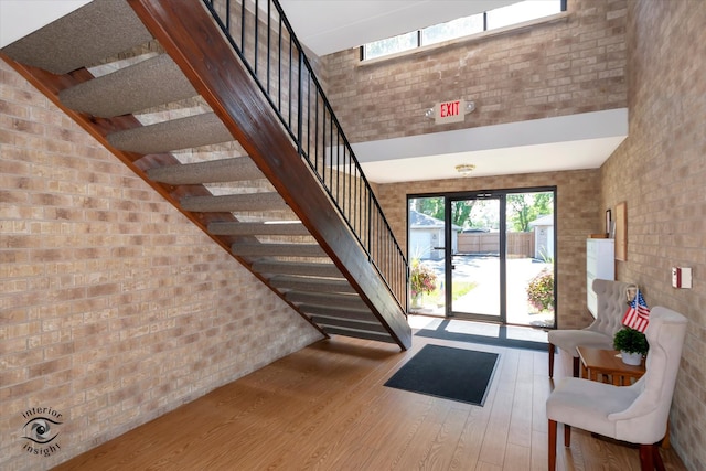 interior space featuring a towering ceiling, brick wall, and hardwood / wood-style flooring