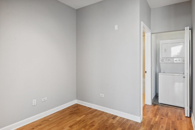 unfurnished room with stacked washer / dryer, light wood-style flooring, and baseboards