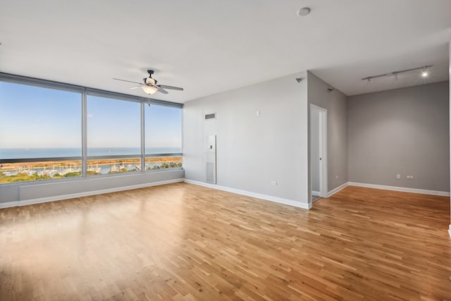 unfurnished room featuring wood-type flooring, a water view, ceiling fan, and rail lighting