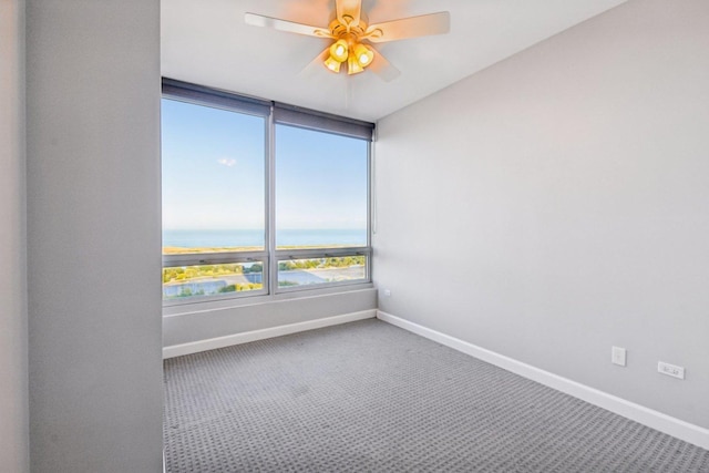 carpeted empty room featuring a ceiling fan, a water view, and baseboards