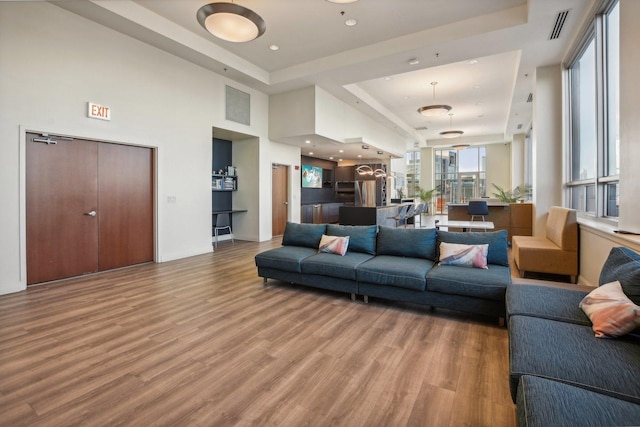 living room featuring a raised ceiling, visible vents, and wood finished floors