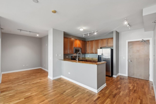 kitchen featuring light wood finished floors, a peninsula, brown cabinetry, stainless steel appliances, and baseboards