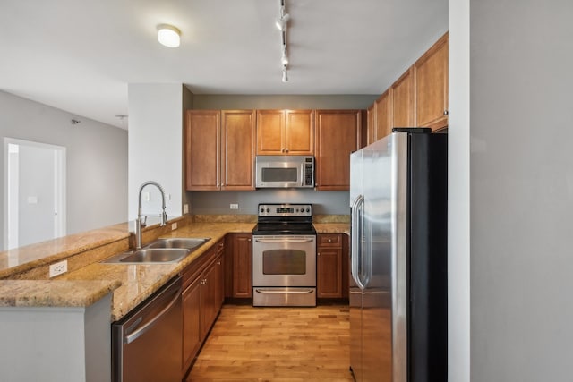 kitchen featuring light stone counters, sink, kitchen peninsula, light hardwood / wood-style flooring, and appliances with stainless steel finishes