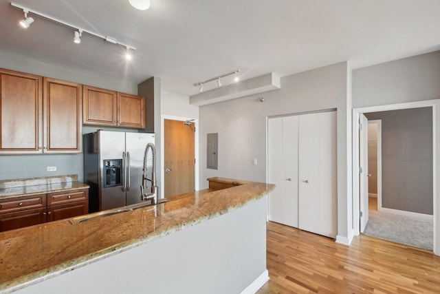 kitchen featuring electric panel, light stone counters, brown cabinets, light wood-type flooring, and stainless steel refrigerator with ice dispenser