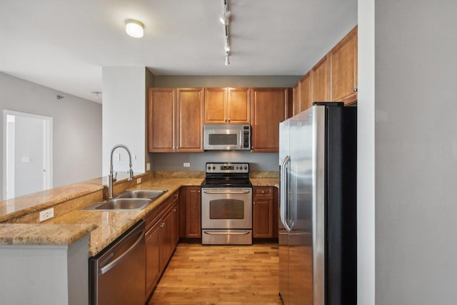 kitchen with a peninsula, appliances with stainless steel finishes, a sink, light wood-type flooring, and light stone counters