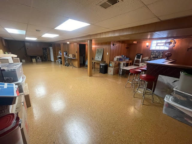 basement with wood walls, bar area, and a paneled ceiling