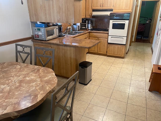 kitchen with light tile patterned floors, sink, kitchen peninsula, white appliances, and extractor fan