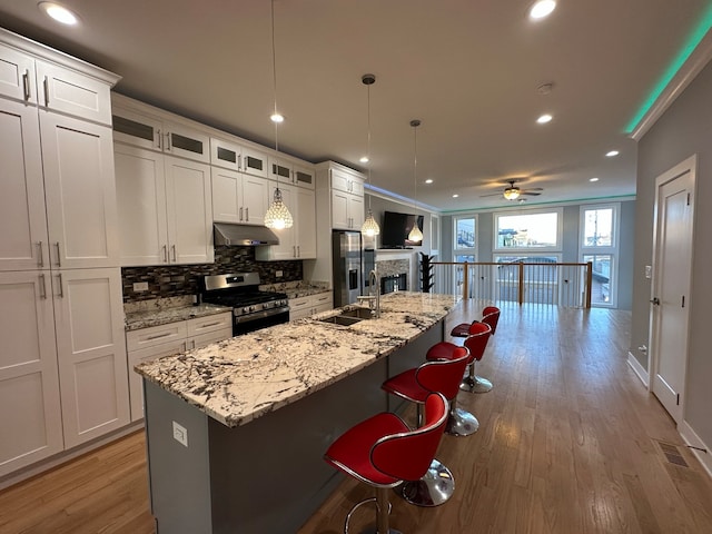 kitchen featuring pendant lighting, a kitchen island with sink, sink, stainless steel gas stove, and ceiling fan