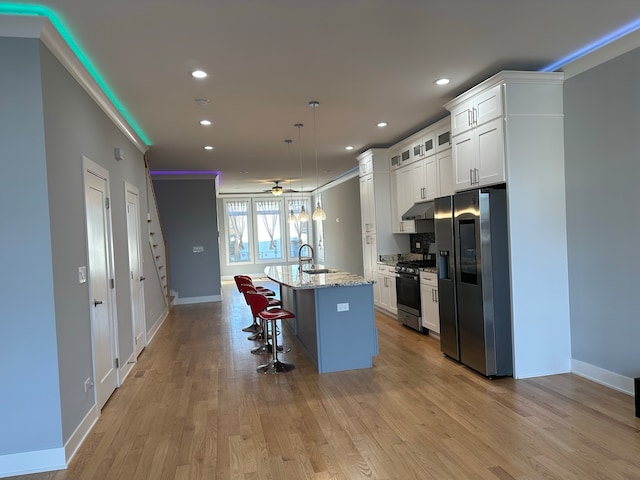 kitchen with white cabinets, stainless steel appliances, light hardwood / wood-style flooring, a kitchen island with sink, and sink