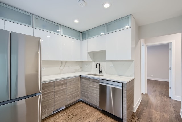 kitchen with light wood-type flooring, sink, white cabinetry, backsplash, and appliances with stainless steel finishes