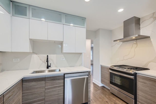 kitchen with tasteful backsplash, white cabinets, stainless steel appliances, sink, and wall chimney range hood