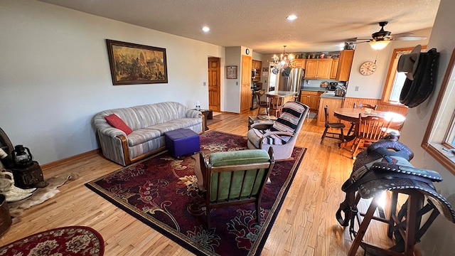 living room featuring a textured ceiling, ceiling fan with notable chandelier, and light hardwood / wood-style floors