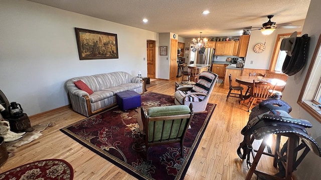 living area with a textured ceiling, baseboards, ceiling fan with notable chandelier, recessed lighting, and light wood-style flooring
