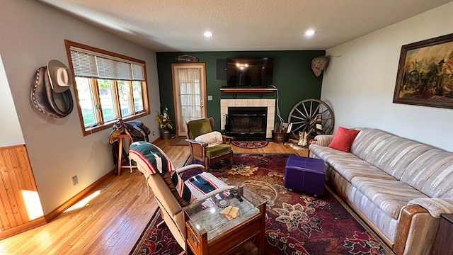 living room with a textured ceiling, a tiled fireplace, and hardwood / wood-style floors