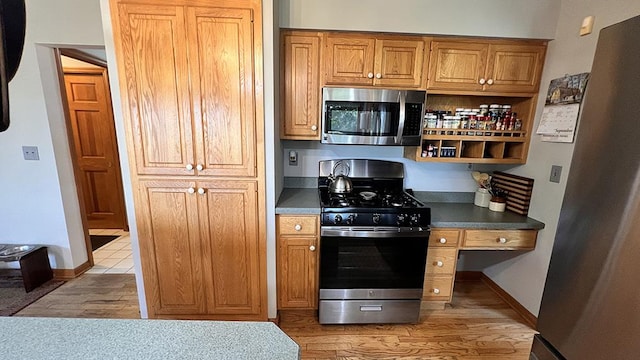 kitchen with dark countertops, baseboards, brown cabinets, light wood-style flooring, and appliances with stainless steel finishes
