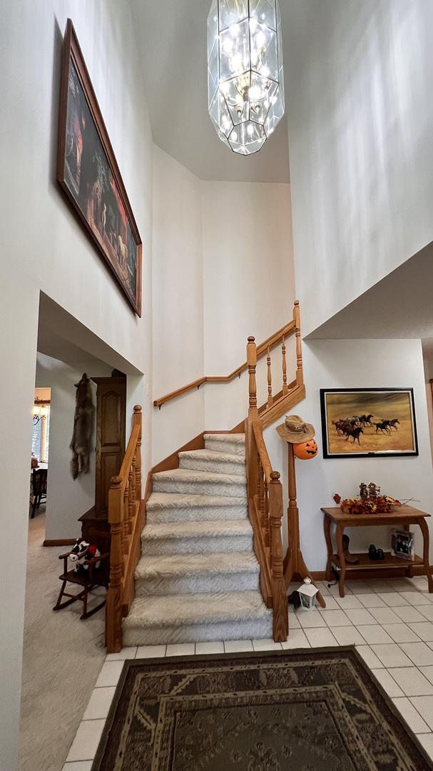stairway featuring tile patterned flooring, a high ceiling, baseboards, and a notable chandelier