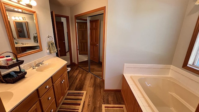 bathroom featuring a garden tub, a sink, wood finished floors, and double vanity