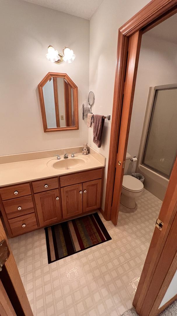 bathroom with tile patterned floors, vanity, combined bath / shower with glass door, toilet, and a chandelier