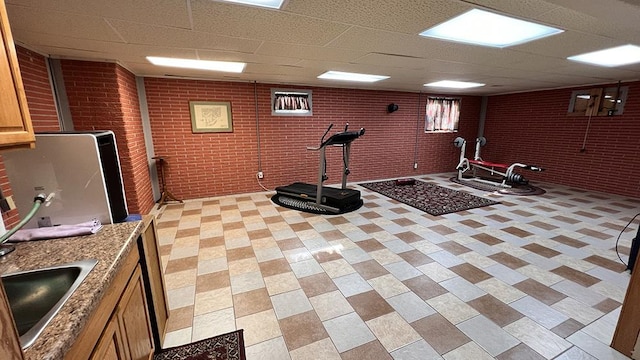 workout area featuring a sink, a paneled ceiling, and brick wall