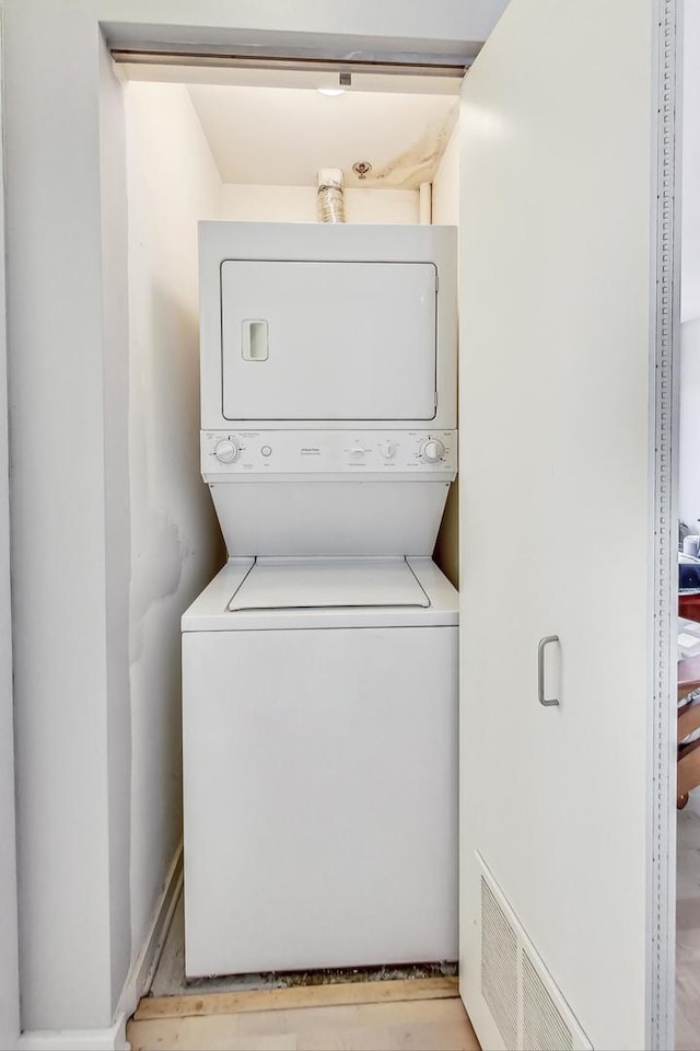 laundry room featuring light wood-type flooring and stacked washer / drying machine