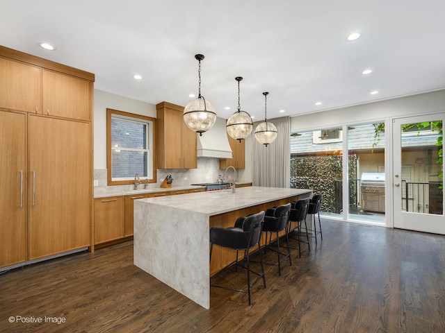 kitchen featuring light stone counters, pendant lighting, an island with sink, backsplash, and dark hardwood / wood-style floors