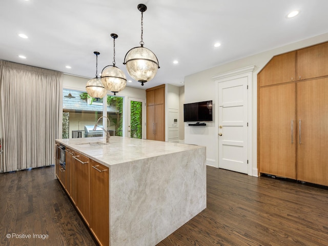 kitchen with dark wood-type flooring, light stone countertops, pendant lighting, sink, and a spacious island