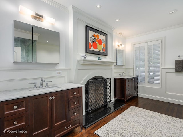 bathroom with a sink, ornamental molding, a fireplace with raised hearth, and wood finished floors