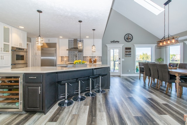 kitchen with wine cooler, white cabinets, wall chimney exhaust hood, a skylight, and stainless steel built in fridge