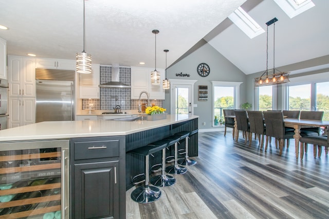 kitchen featuring white cabinets, pendant lighting, beverage cooler, wall chimney range hood, and stainless steel appliances