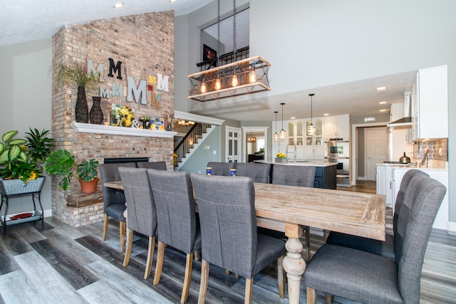 dining room featuring a chandelier, dark hardwood / wood-style floors, high vaulted ceiling, and a brick fireplace