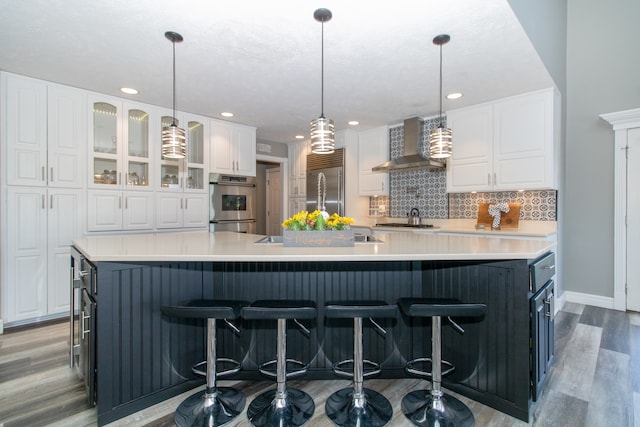 kitchen with white cabinets, a large island, and wall chimney range hood