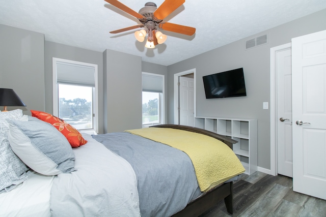 bedroom featuring a textured ceiling, ceiling fan, multiple windows, and dark hardwood / wood-style flooring