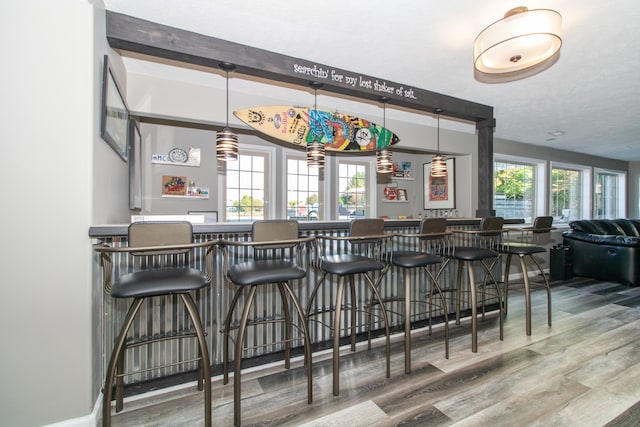 bar featuring wood-type flooring, beam ceiling, a textured ceiling, and decorative light fixtures