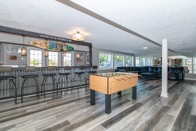 game room featuring wood-type flooring, a textured ceiling, a healthy amount of sunlight, and bar