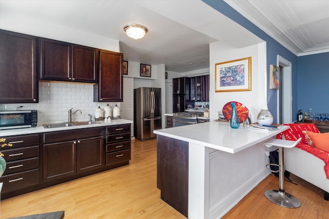 kitchen with sink, kitchen peninsula, stainless steel appliances, a breakfast bar area, and light hardwood / wood-style floors