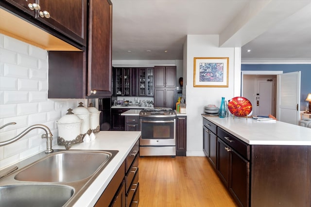 kitchen with light wood-type flooring, stainless steel range with gas cooktop, sink, decorative backsplash, and crown molding