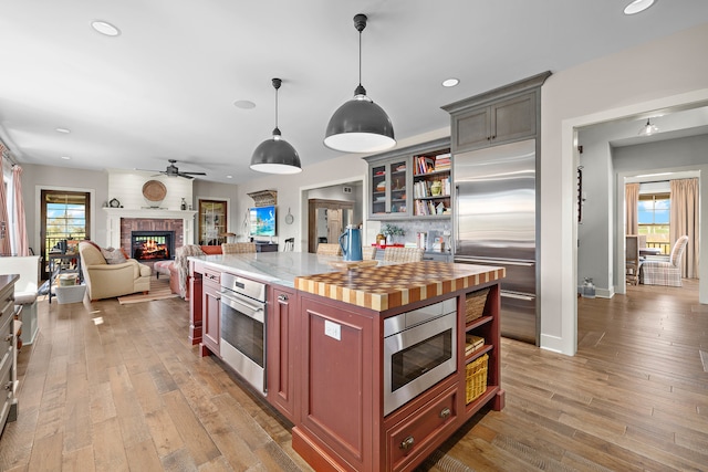 kitchen featuring built in appliances, hanging light fixtures, a fireplace, light hardwood / wood-style floors, and ceiling fan